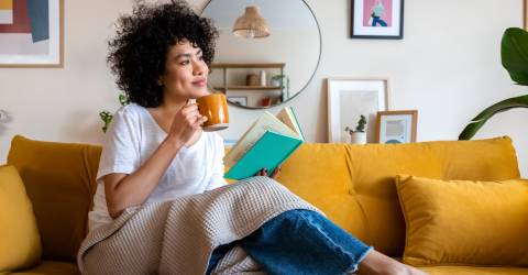 Een ontspannen Afro-Amerikaanse vrouw leest thuis een boek en drinkt koffie op de bank